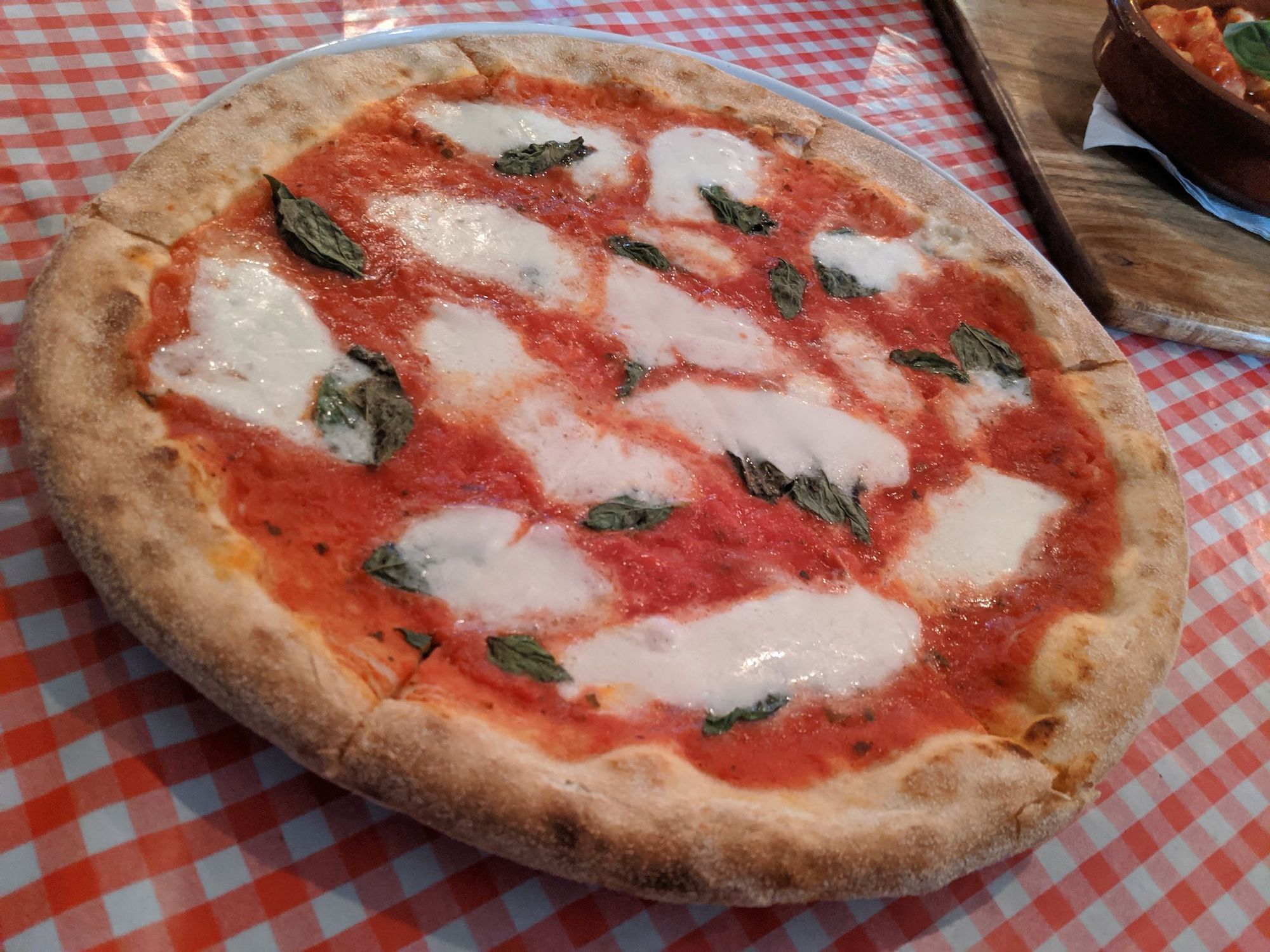Margherita Pizza on chequered tablecloth. Generous cheese and puffy crust.