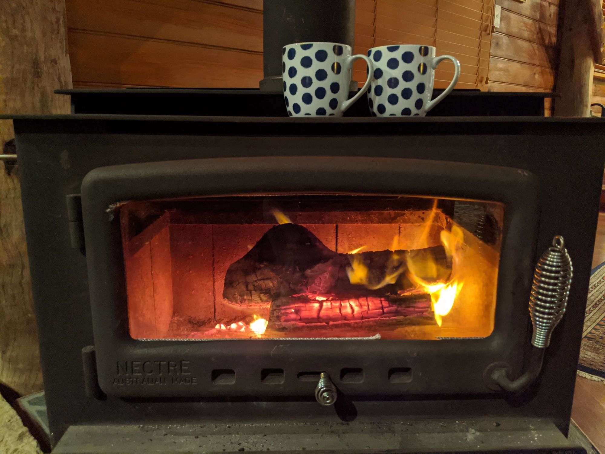 Fireplace with wood burning, mugs above the fireplace.