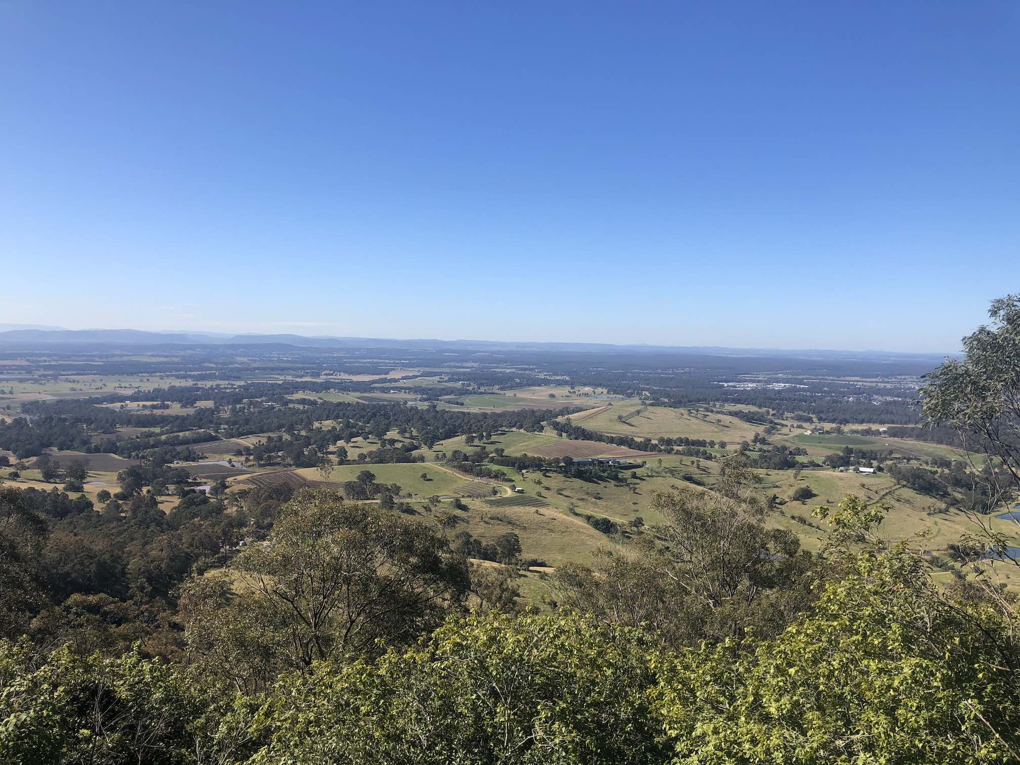 Looking down over farmland from about 300m high, blue sky, flat horizon in the distance.