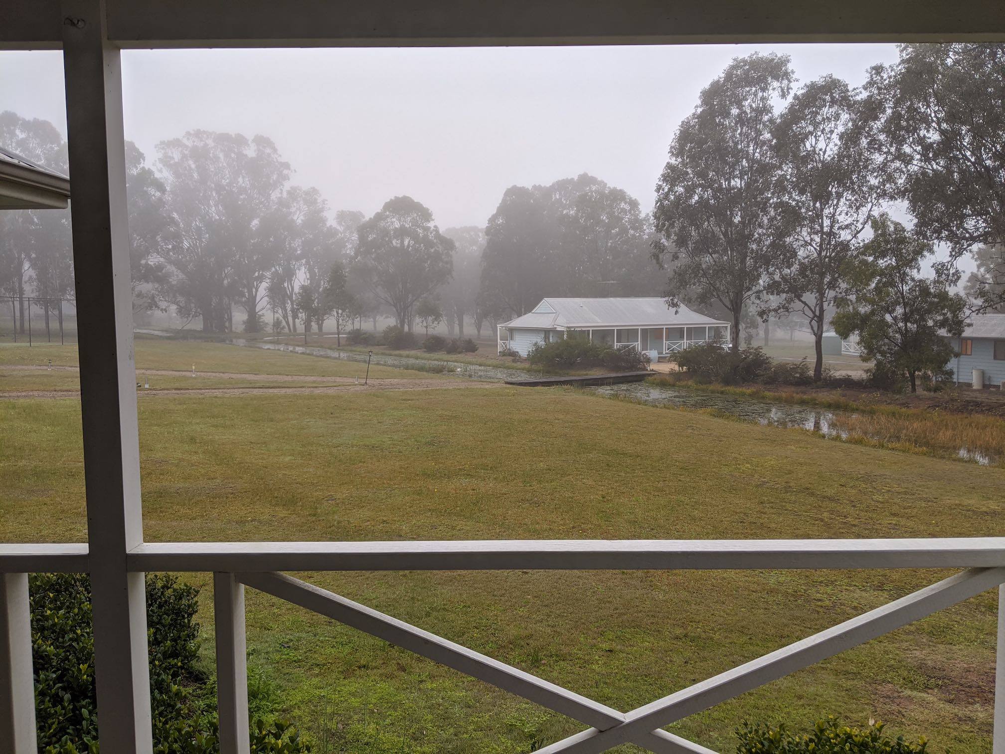 Low cloud and rain over grassy field with houses in it.