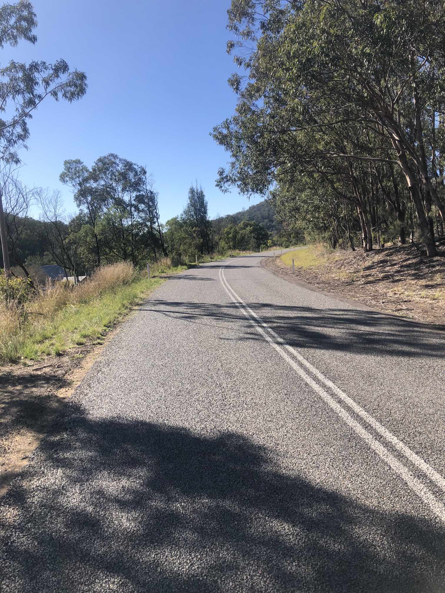 A narrow two lane road with no shoulder veering right around a corner.