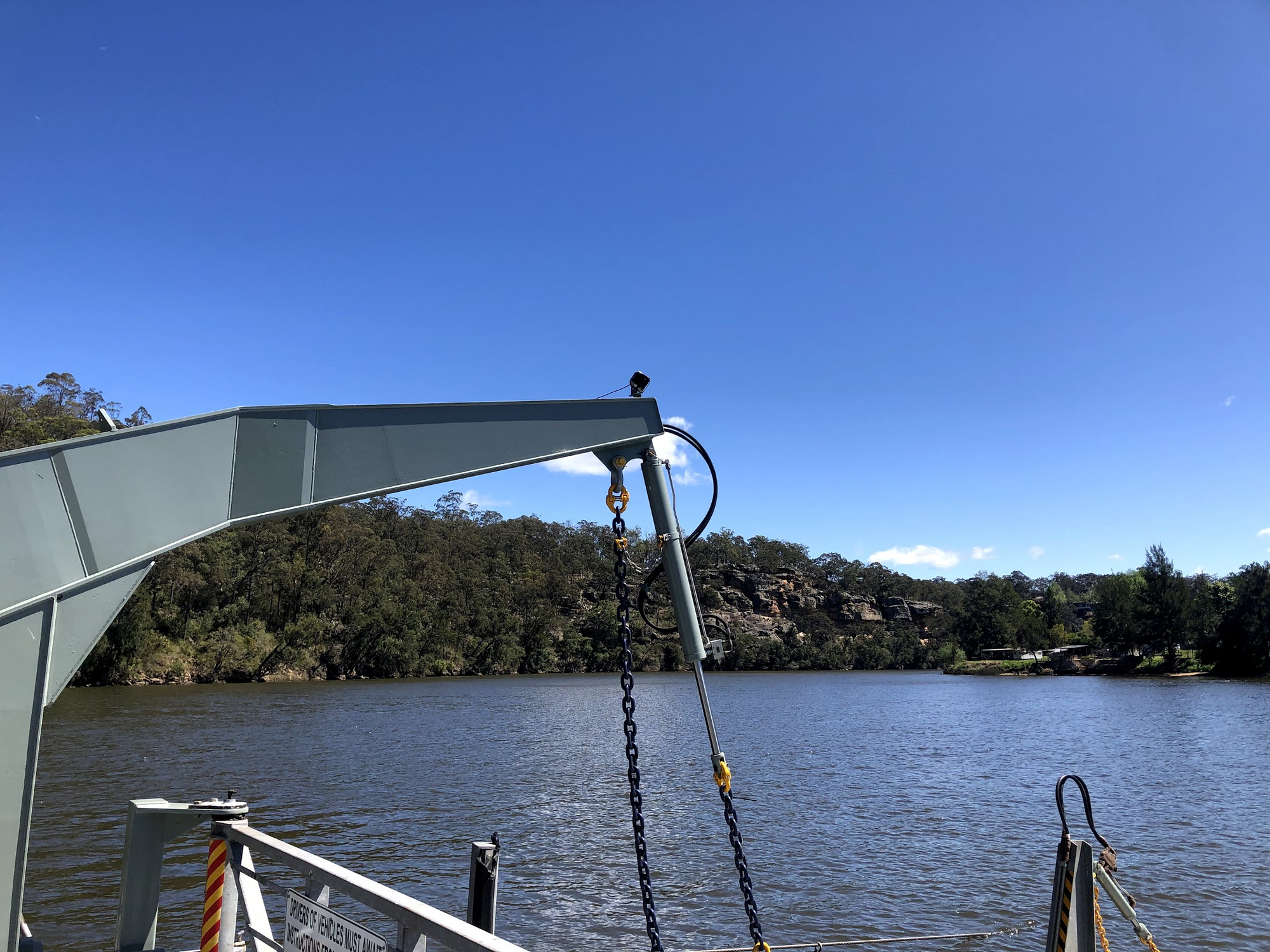 Blue sky, sandstone cliff above river water, taken from onboard a small car ferry.